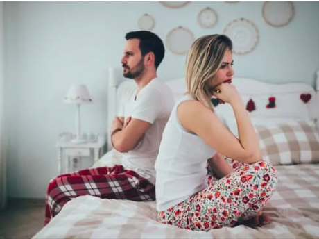 Couple sitting on bed angry, backs turned, marriage failing.