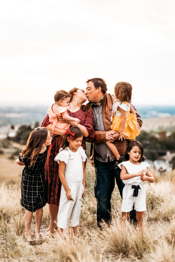 Saving Marriage from Parenthood: Couple kissing while five kids surround them. 